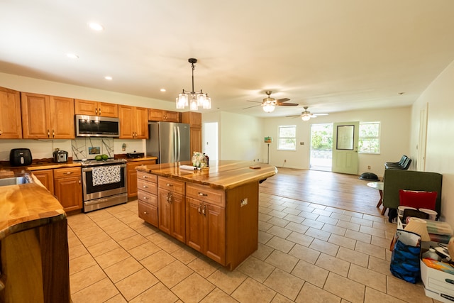 kitchen with ceiling fan with notable chandelier, stainless steel appliances, a center island, decorative light fixtures, and wood counters