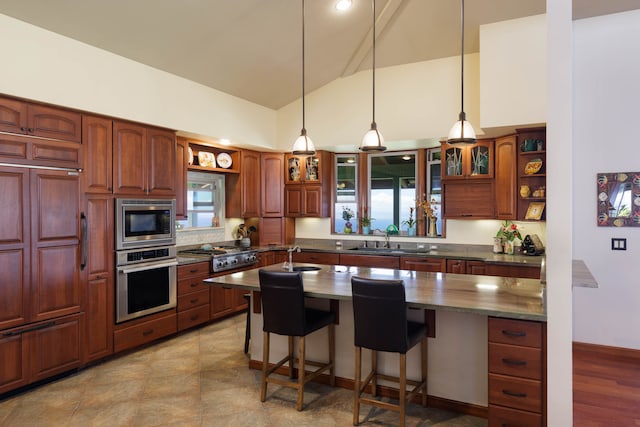 kitchen with appliances with stainless steel finishes, high vaulted ceiling, pendant lighting, sink, and a breakfast bar area