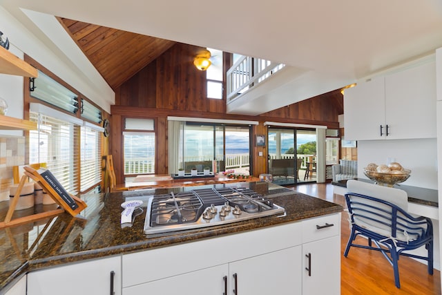 kitchen featuring white cabinets, high vaulted ceiling, wooden walls, and stainless steel gas cooktop