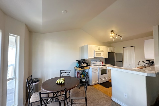 kitchen featuring white appliances, light hardwood / wood-style flooring, vaulted ceiling, kitchen peninsula, and white cabinets