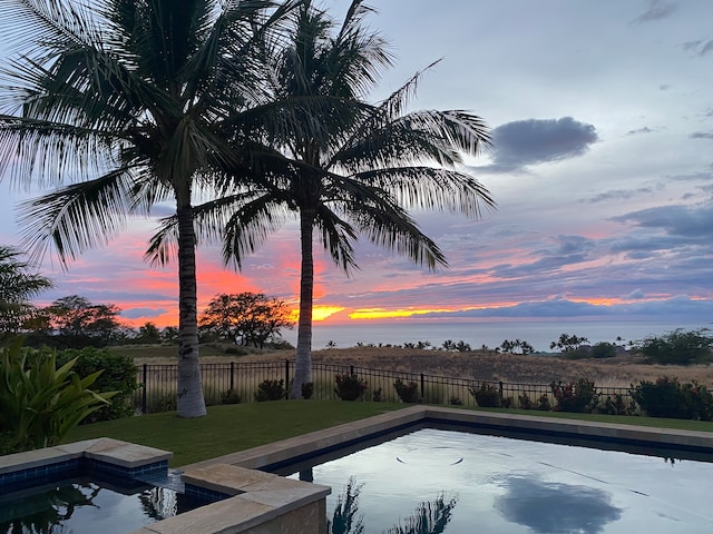 pool at dusk featuring a water view and a yard