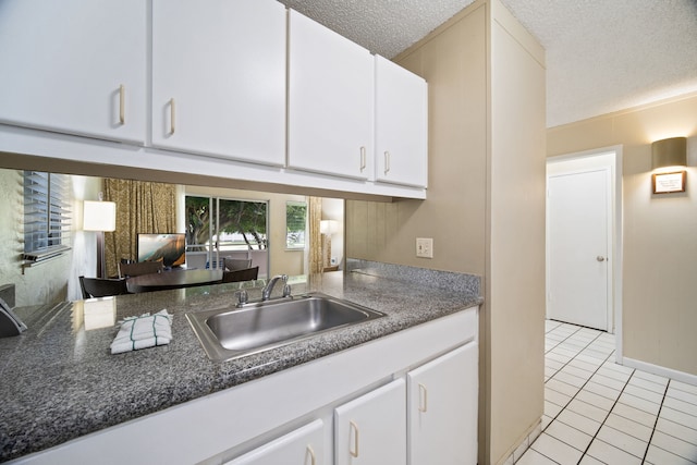 kitchen with light tile patterned floors, a textured ceiling, sink, and white cabinets