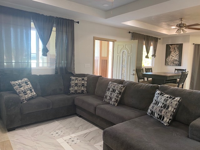 living room featuring ceiling fan, a raised ceiling, and a wealth of natural light