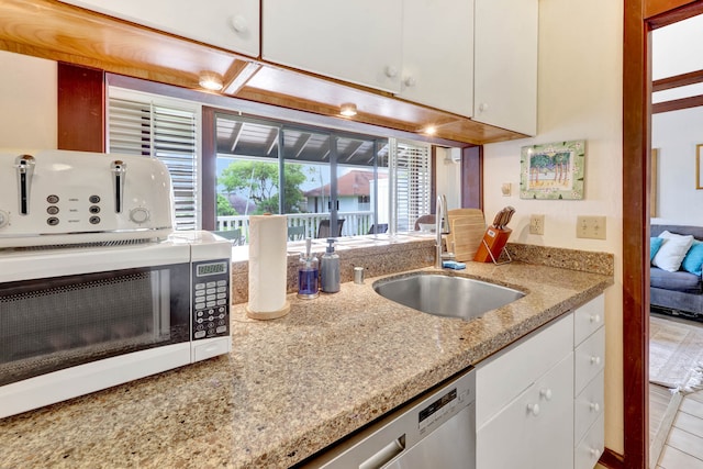 kitchen featuring light stone counters, stainless steel dishwasher, sink, light tile patterned flooring, and white cabinetry