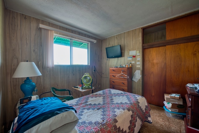 bedroom featuring carpet flooring, wooden walls, and a textured ceiling