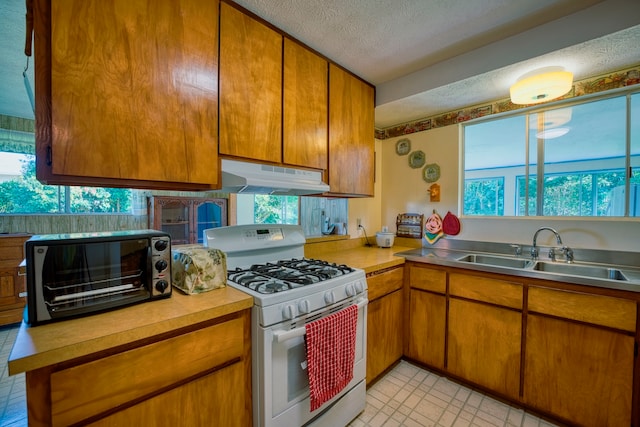 kitchen featuring white range with gas stovetop, a textured ceiling, a healthy amount of sunlight, and sink