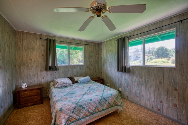 carpeted bedroom with multiple windows, wood walls, and ceiling fan