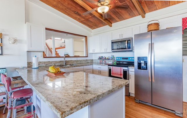 kitchen with white cabinets, kitchen peninsula, appliances with stainless steel finishes, a kitchen bar, and vaulted ceiling with beams