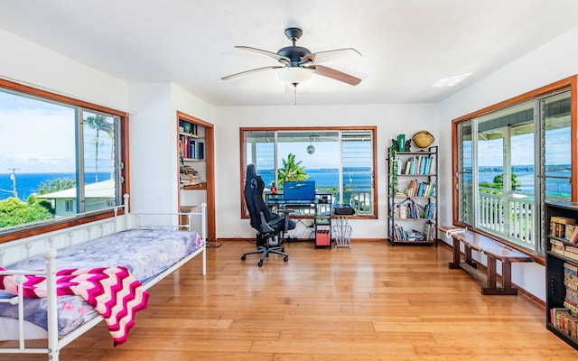 bedroom with a water view, light hardwood / wood-style flooring, multiple windows, and ceiling fan