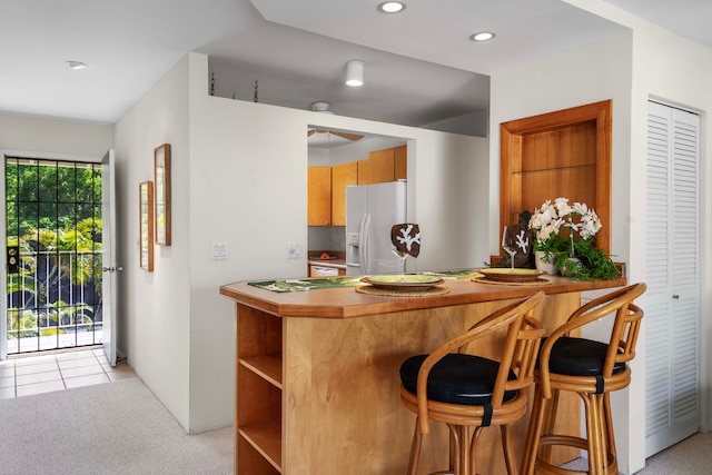 kitchen with light carpet, white refrigerator with ice dispenser, kitchen peninsula, and a kitchen breakfast bar