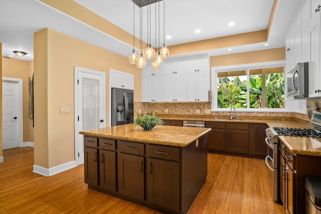 kitchen featuring a kitchen island, white cabinetry, light wood-type flooring, appliances with stainless steel finishes, and decorative light fixtures