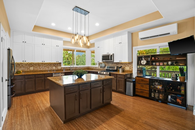 kitchen with a center island, stainless steel appliances, hanging light fixtures, a wall unit AC, and light hardwood / wood-style flooring