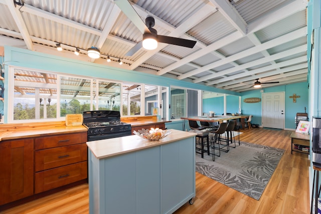 kitchen featuring rail lighting, light hardwood / wood-style floors, black gas stove, vaulted ceiling with beams, and a center island