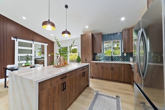 kitchen with a barn door, a center island, stainless steel fridge, light hardwood / wood-style floors, and pendant lighting