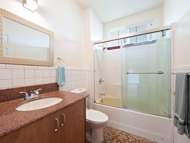 full bathroom with vanity, toilet, combined bath / shower with glass door, and tile walls