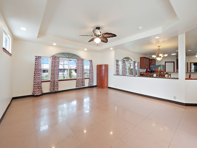 tiled empty room with a raised ceiling, ceiling fan with notable chandelier, and plenty of natural light