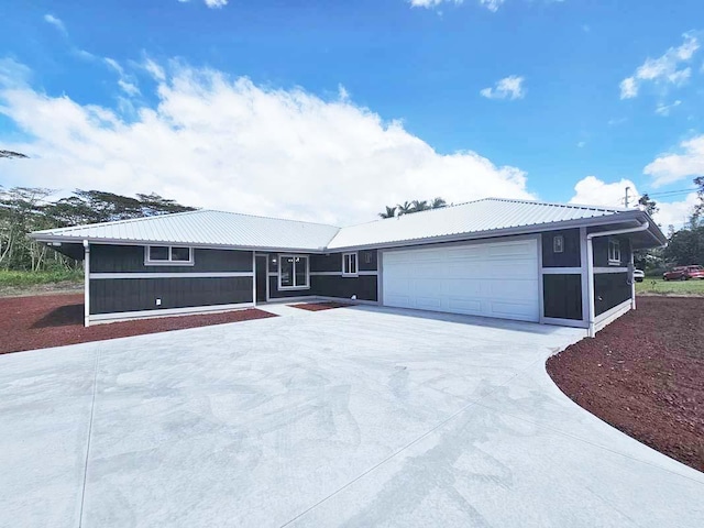 ranch-style home featuring a garage, driveway, and metal roof