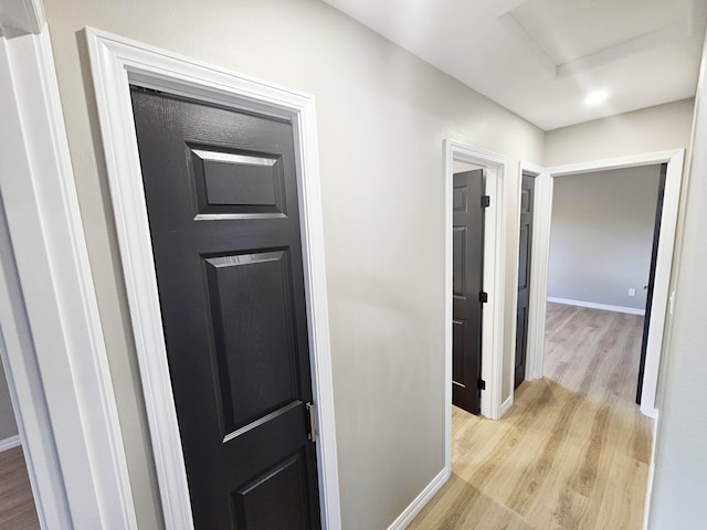 hallway featuring baseboards, attic access, and light wood-style flooring