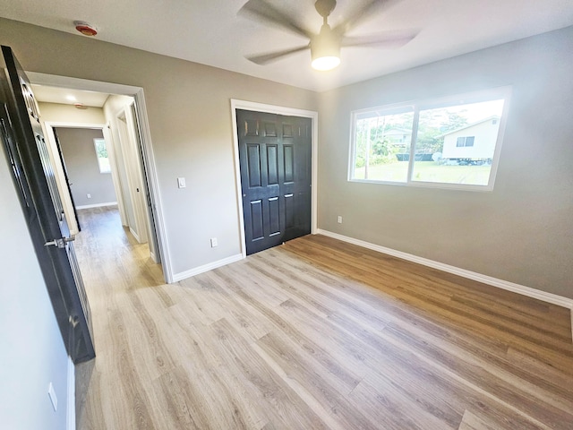 unfurnished bedroom with baseboards, a ceiling fan, a closet, and light wood-style flooring