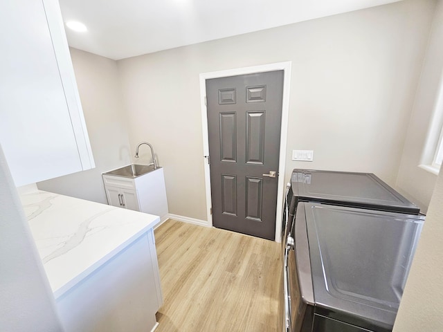 laundry room featuring cabinet space, a sink, separate washer and dryer, baseboards, and light wood-type flooring