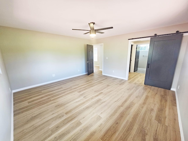 unfurnished bedroom featuring baseboards, a ceiling fan, light wood-type flooring, and a barn door