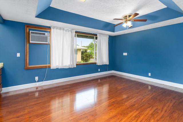 empty room with a tray ceiling, ceiling fan, a textured ceiling, and hardwood / wood-style flooring