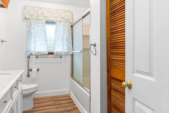 full bathroom with hardwood / wood-style floors, vanity, combined bath / shower with glass door, and toilet