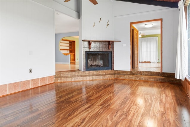 unfurnished living room with wood-type flooring, a healthy amount of sunlight, and a tiled fireplace