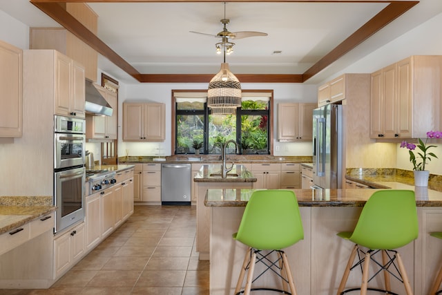 kitchen with wall chimney exhaust hood, light brown cabinetry, a kitchen breakfast bar, light stone counters, and stainless steel appliances