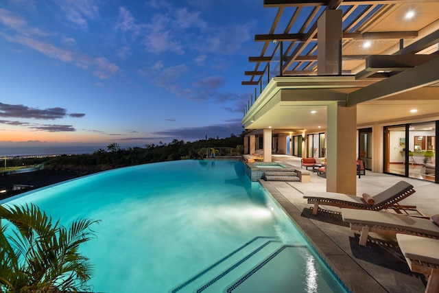 pool at dusk featuring an in ground hot tub and a patio area