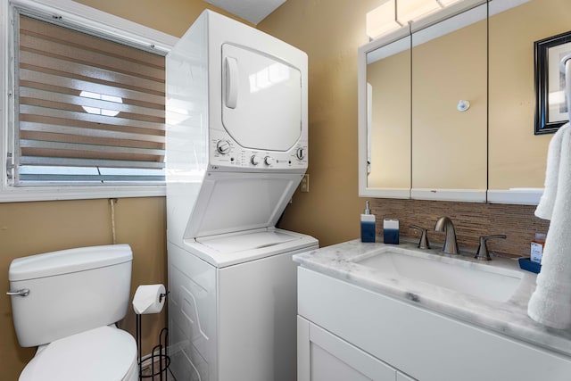 bathroom with tasteful backsplash, stacked washer and clothes dryer, vanity, and toilet