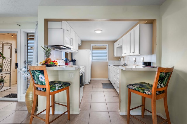 kitchen featuring white cabinets, light tile patterned floors, sink, kitchen peninsula, and a breakfast bar area