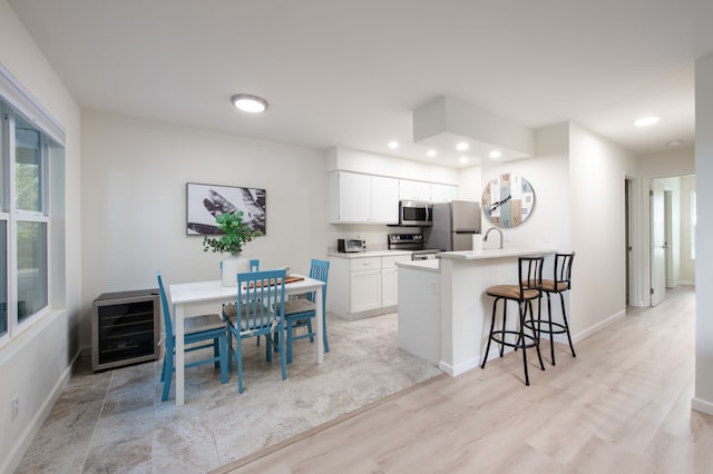 kitchen featuring white cabinets, light hardwood / wood-style floors, kitchen peninsula, appliances with stainless steel finishes, and a kitchen bar