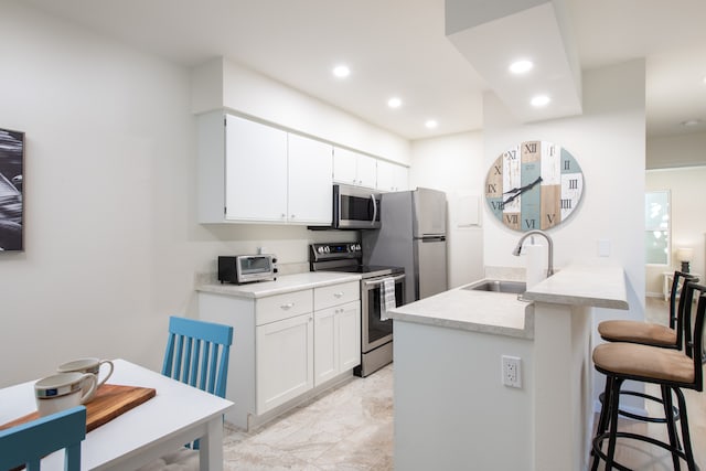 kitchen featuring stainless steel appliances, white cabinets, sink, kitchen peninsula, and a kitchen breakfast bar