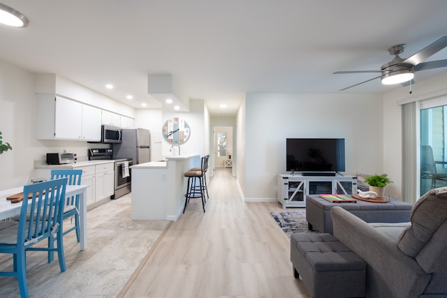 kitchen featuring ceiling fan, white cabinets, stainless steel appliances, a breakfast bar, and light wood-type flooring