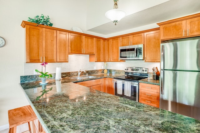 kitchen with appliances with stainless steel finishes, sink, pendant lighting, dark stone countertops, and a breakfast bar area