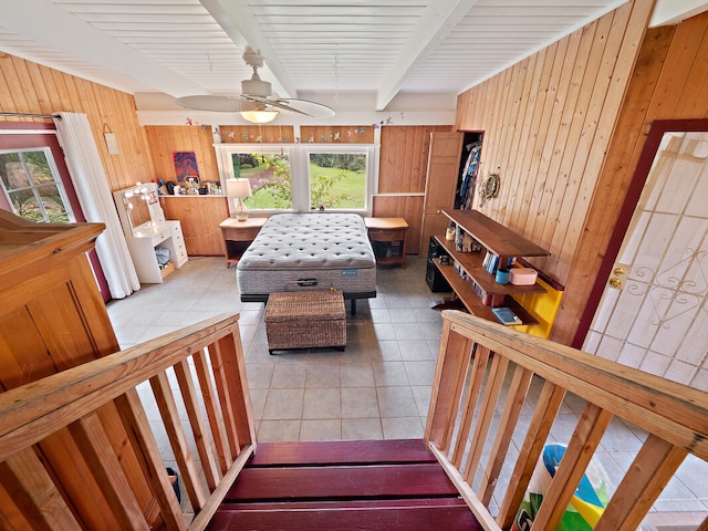 interior space with light tile patterned flooring, beam ceiling, wooden walls, and ceiling fan