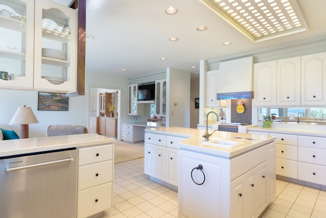 kitchen with premium range hood, sink, stainless steel dishwasher, an island with sink, and white cabinets