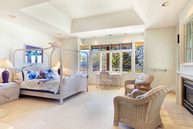 bedroom featuring light colored carpet, a textured ceiling, and a tray ceiling