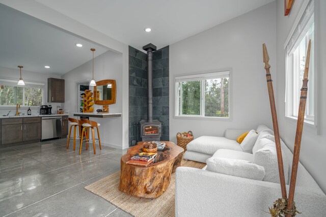 living room featuring plenty of natural light, a wood stove, sink, and lofted ceiling