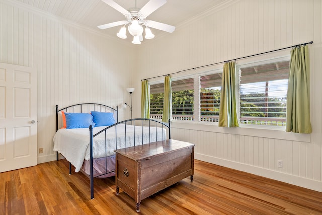 bedroom featuring ceiling fan, hardwood / wood-style flooring, ornamental molding, and wooden walls