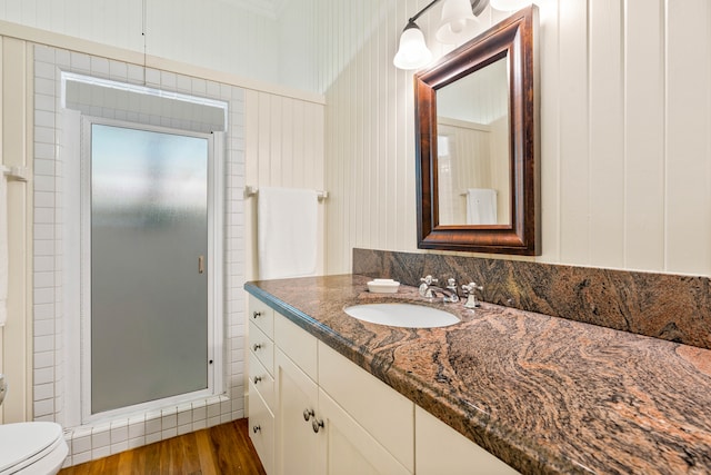 bathroom featuring hardwood / wood-style floors, a shower with door, toilet, vanity, and wooden walls