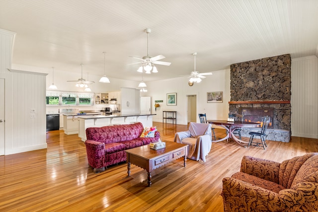 living room with ceiling fan, a stone fireplace, and light wood-type flooring