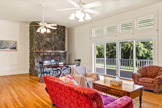 living room featuring crown molding, light hardwood / wood-style flooring, a stone fireplace, and ceiling fan