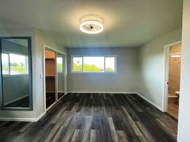 unfurnished bedroom featuring dark wood-type flooring, a textured ceiling, multiple windows, and a closet