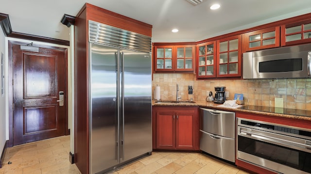 kitchen featuring appliances with stainless steel finishes, light stone countertops, sink, and backsplash