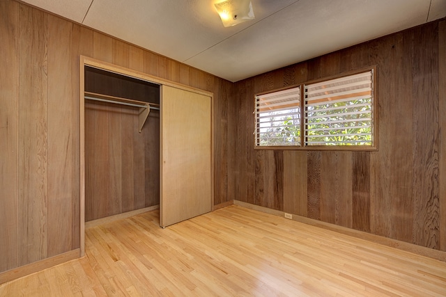 unfurnished bedroom with a closet, light hardwood / wood-style floors, and wood walls