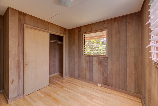 unfurnished bedroom with light hardwood / wood-style flooring, a closet, and wooden walls