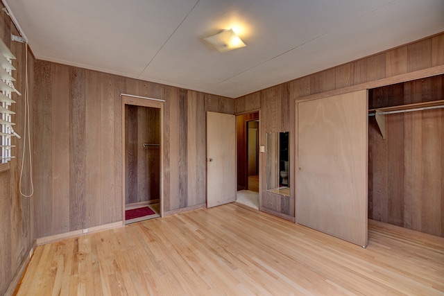 unfurnished bedroom with a closet, wooden walls, and light wood-type flooring