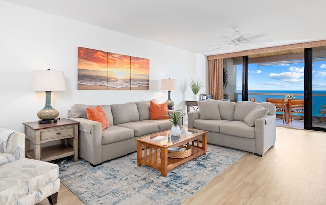 living room with a water view, ceiling fan, light wood-type flooring, and floor to ceiling windows